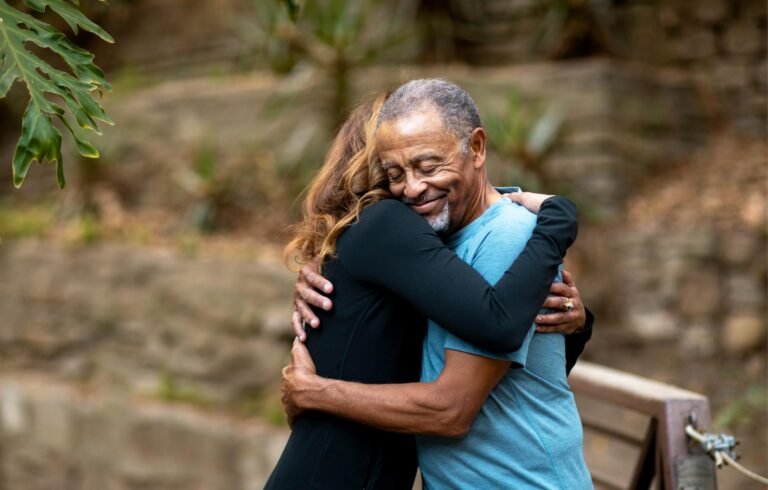 Senior people hug outdoors.