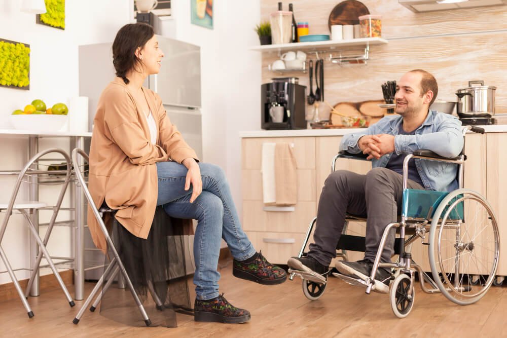 wife talks with wheelchair-bound husband in kitchen