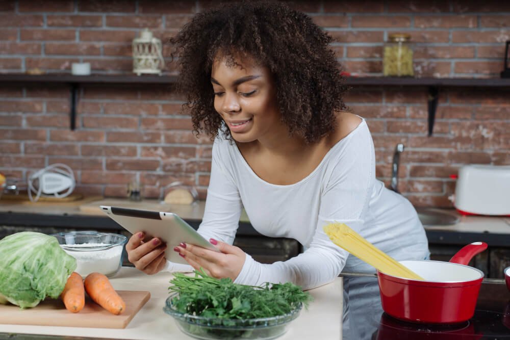 Caregiver prepares a nutritious meal with tablet in hand.