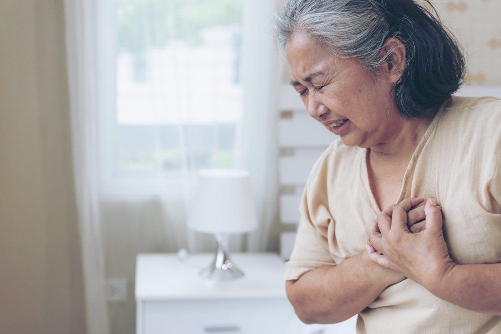 Senior Asian woman clutches chest from pain