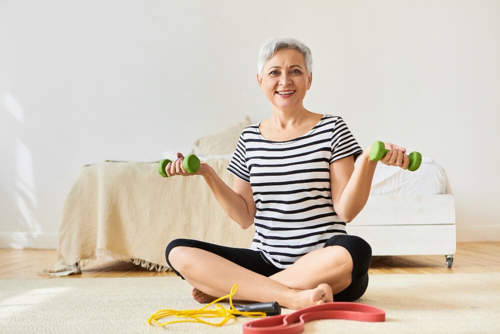 Senior woman sits on floor with dumbbells in hand