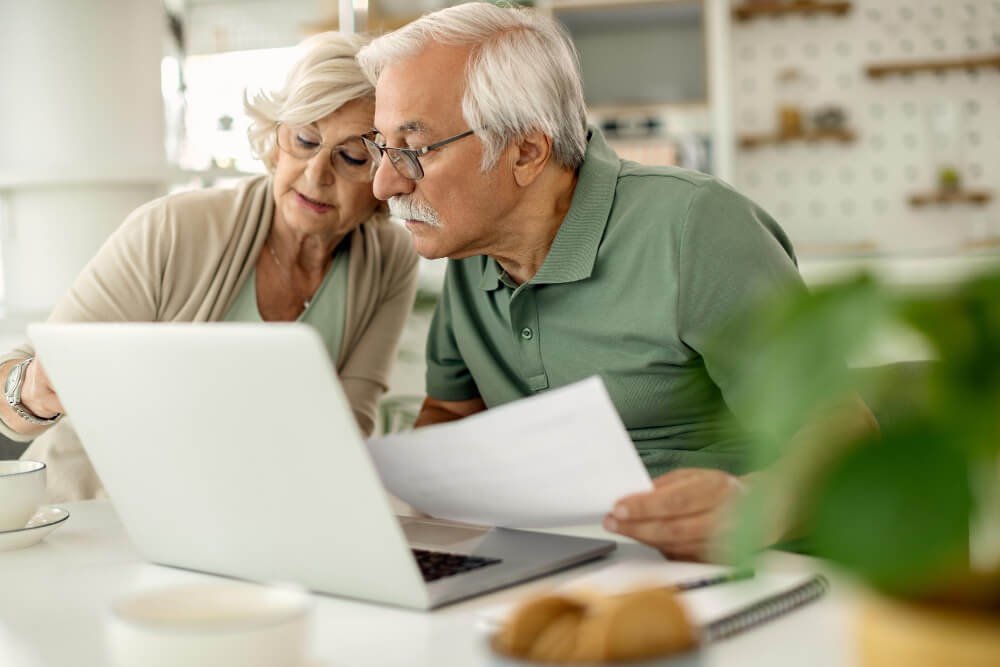 Senior couple sits at laptop while reviewing their budget.