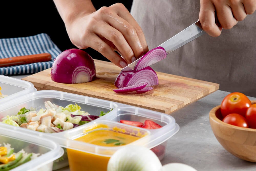 Caregiver slicing onions with food containers in foreground