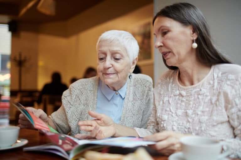 woman sits with her elderly mother and looks at photo album
