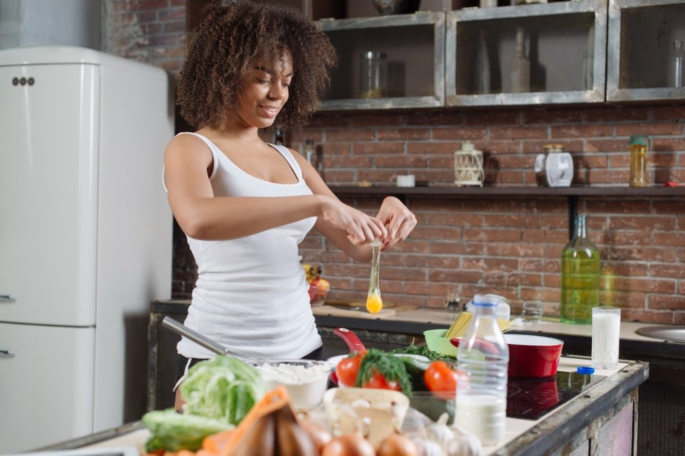Young woman cracks an egg while batch cooking