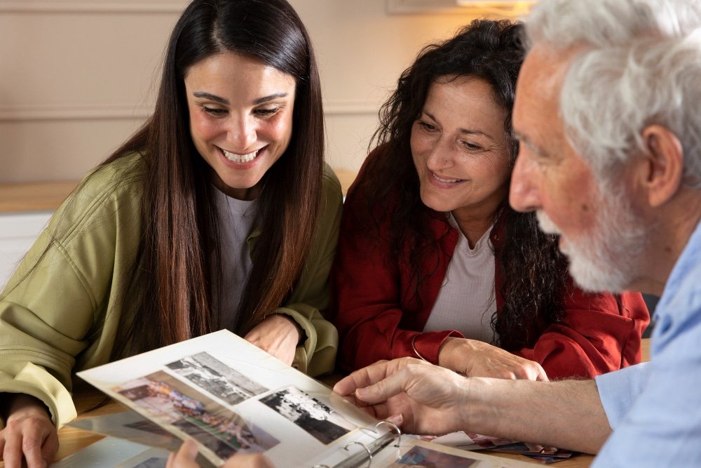 two daughters look at a photo album with their elderly father