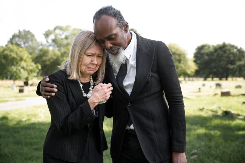 Senior man hugs senior woman at grave site