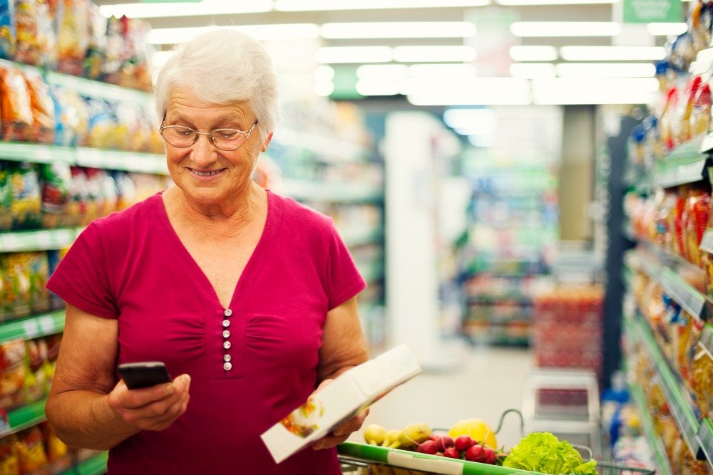 senior woman uses app while grocery shopping